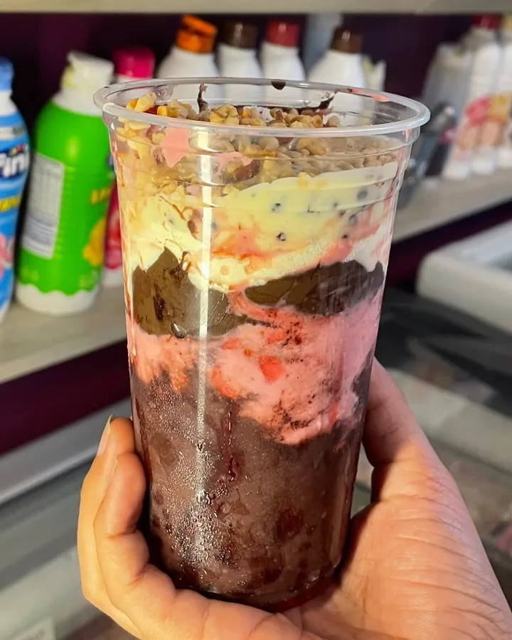 Copo de açaí em camadas com granola e creme, segurado na mão